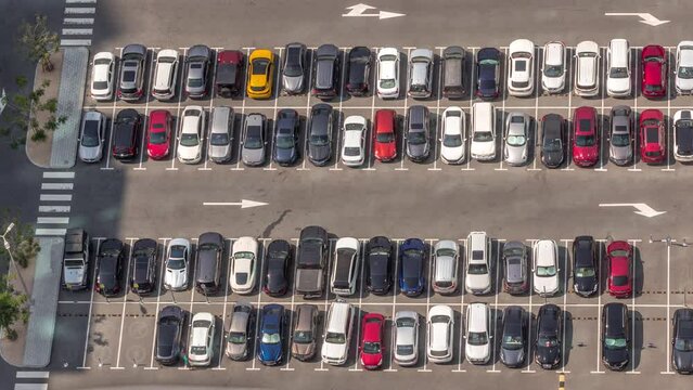 Aerial view of many colorful cars parked on parking lot with lines and markings for places and directions during all day timelapse with long shadows moving fast. Dubai financial district avenue