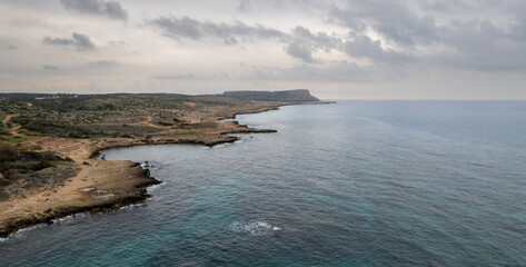 Drone aerial rocky coastline at sunset. Stormy sea, cloudy sky.