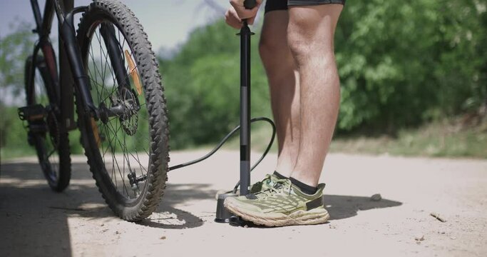 Mountain biker inflates tire on dirt road using a pump beside a car. Emergency repair and trailside maintenance.