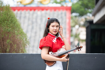 Portrait of Asian young woman play violin with feeling happy and smile in red shirt in city outdoor