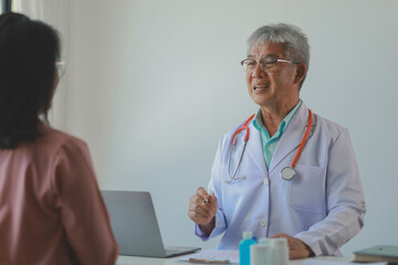male medical practitioner reassuring a patient, Doctor and patient in conversation, Asian male doctor consulting patient, Professional physician wearing white coat talking to mature woman