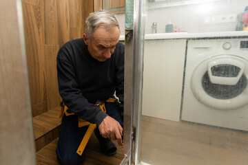 an elderly man repairing door of shower cabin in bathroom
