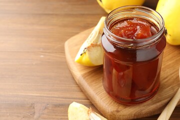 Tasty homemade quince jam in jar and fruits on wooden table, closeup. Space for text