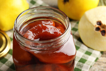 Tasty homemade quince jam in jar and fruits on table, closeup
