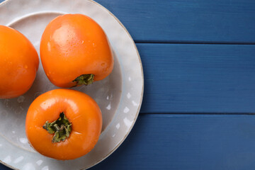 Delicious ripe persimmons on blue wooden table, top view. Space for text