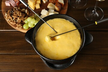 Fondue pot with melted cheese and different products on wooden table, above view