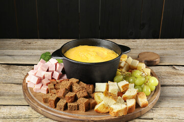 Fondue pot with melted cheese and different products on wooden table