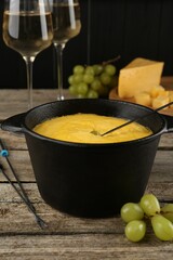 Fondue pot with melted cheese, glasses of wine and different products on wooden table