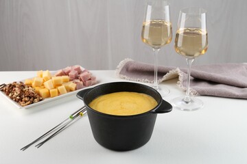 Fondue with tasty melted cheese, forks, different products and aromatic wine in glasses on white table
