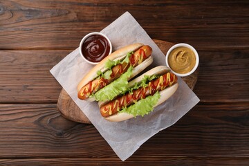 Tasty hot dogs with lettuce, ketchup and mustard on wooden table, top view