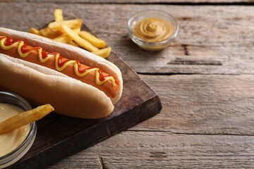Delicious hot dog, sauces and French fries on wooden table, closeup. Space for text