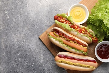 Delicious hot dogs with different toppings served on grey table, flat lay. Space for text - obrazy, fototapety, plakaty