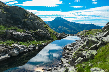 Small high altitude alpine lake surrounded by rocks in High Tauern National Park, Carinthia, Austria. Idyllic hiking trail with panoramic view of mountain ridges in Austrian Alps. Summer in Mallnitz
