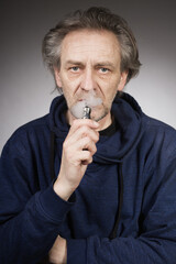 Older man with wrinkles on face skin smoking electronic cigarette