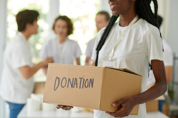 Smiling Black young woman holding box with donated food or clothes