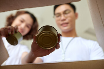 Volunteers putting canned food in box, view from inside the box