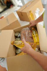 Charity organization volunteer packing canned food, nuts and vegetable oil in box for people in need