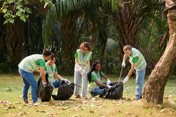 Group of cheerful volunteers picking garbage and fallen leaves in park