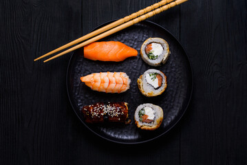 sushi and rolls on a black plate, on a black wooden background, top view