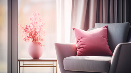 Modern grey armchair with pink decorative pillows and a vase of pink flowers by the window