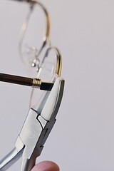 Adjusting inclination of temples on modern metal eyeglass frame with conical inclination pliers equipped with nylon replaceable jaws. - obrazy, fototapety, plakaty