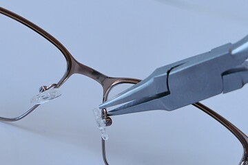 Adjusting nose pads position on metal eyeglass frame with flat snipe nose pliers. 