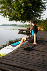 A girl in sportswear ready to paddleboard on a serene lake, surrounded by lush greenery.