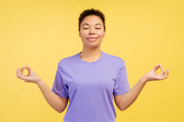 Young African American woman, performing yoga pose with eyes shut, set against a yellow background