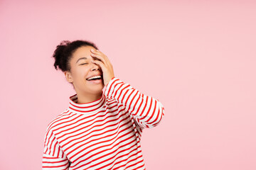 Laughing young African American woman in striped shirt, covering face with hand, engulfed in giggles