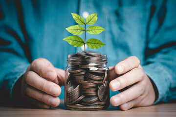 Businessman holding full money saving jar with green leafs plant growing for money deposit saving...