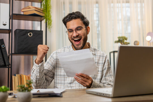 Happy Indian young businessman manager open envelope letter, reading it. Career growth advance promotion, bank loan approval, successful admission to monetary award, long-awaited invitation great news