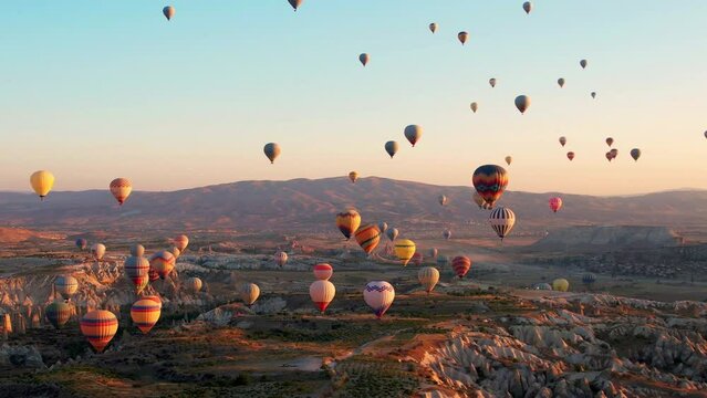 Aerial view of many colorful hot air balloons fly in the sky over a mountain valley at summer sunrise in Cappadocia, Turkey.