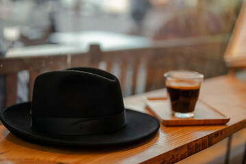 A cup of coffee on a bar with a gentleman's hat next to it. 