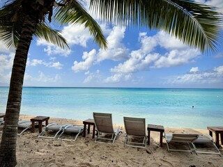 view of a sandy caribbean beach with deck chairs on the sand and turquoise colored sea on a...
