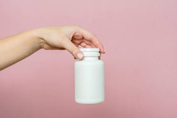 Bottle of pills or vitamins in woman's hand. White packaging for your pill or capsule and supplement