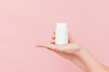 White bottle plastic tube in woman's hands on pink background. Packaging for pills, capsules or...