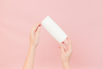 Shampoo, hair conditioner or body lotion bottle in hands in pink background. Cosmetics bottle
