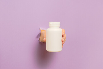 Cool view on white bottle plastic tube in hands on lilac background. Packaging for pills, capsules or supplements. Cosmetics