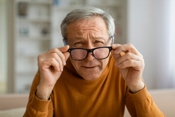 Tired elderly man removing eyeglasses, home interior