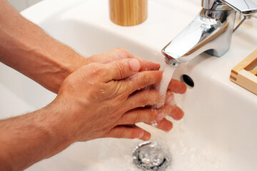 Man washes his hands with soap under the water tap