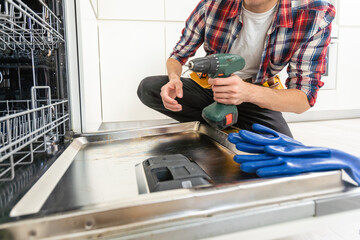 Process of dishwashing machine installation. Young African service man setting up dishwasher in new stylish kitchen. Diverce handyman in workwear, close portrait.