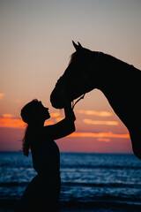 A girl and her horse on the beach during sunset