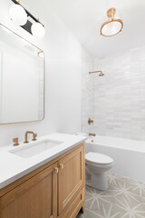 A bathroom with an oak cabinet, white marble countertop, pattern tile floor, and gold light...