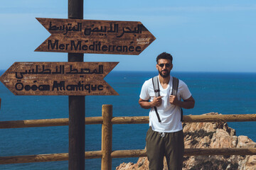 A man standing in front of the sign depicting the point where the Mediterranean and the Atlantic...