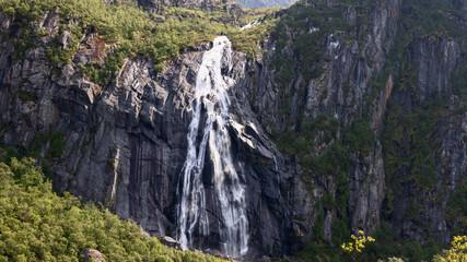 A powerful cascade, Valefossen, cuts through the rugged cliffs surrounded by the lush greenery of Norway's Lofoten Islands.