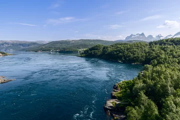 Fotobehang Vibrant greenery flanks the world-renowned Saltstraumen, where powerful water currents dance between Norwegian fjords under a blue sky © Artem