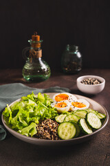 Bowl with quinoa, cucumber, boiled egg, lettuce and sesame seeds on the table vertical view