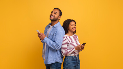 Dreamy black couple standing back to back and holding their mobile phones