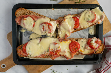 Baked baguette sandwich with italian ham, mozzarella cheese, tomatoes and thyme on rustic bread