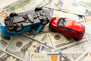 concept of car accident loss and damage. two model cars on the heap of us hundred dollars. 